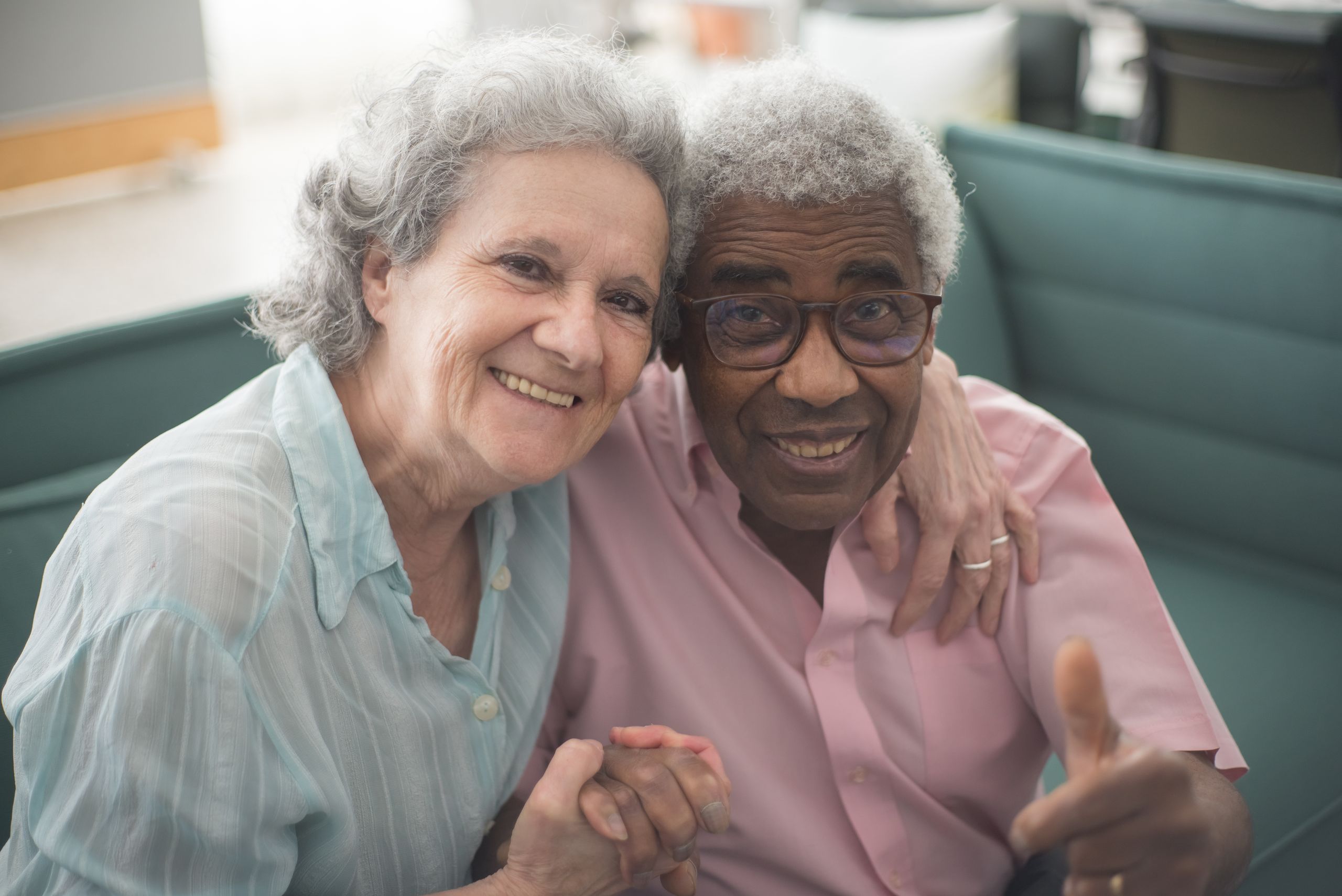 Elderly couple sharing a joyful moment indoors, sitting together on a couch with loving expressions.